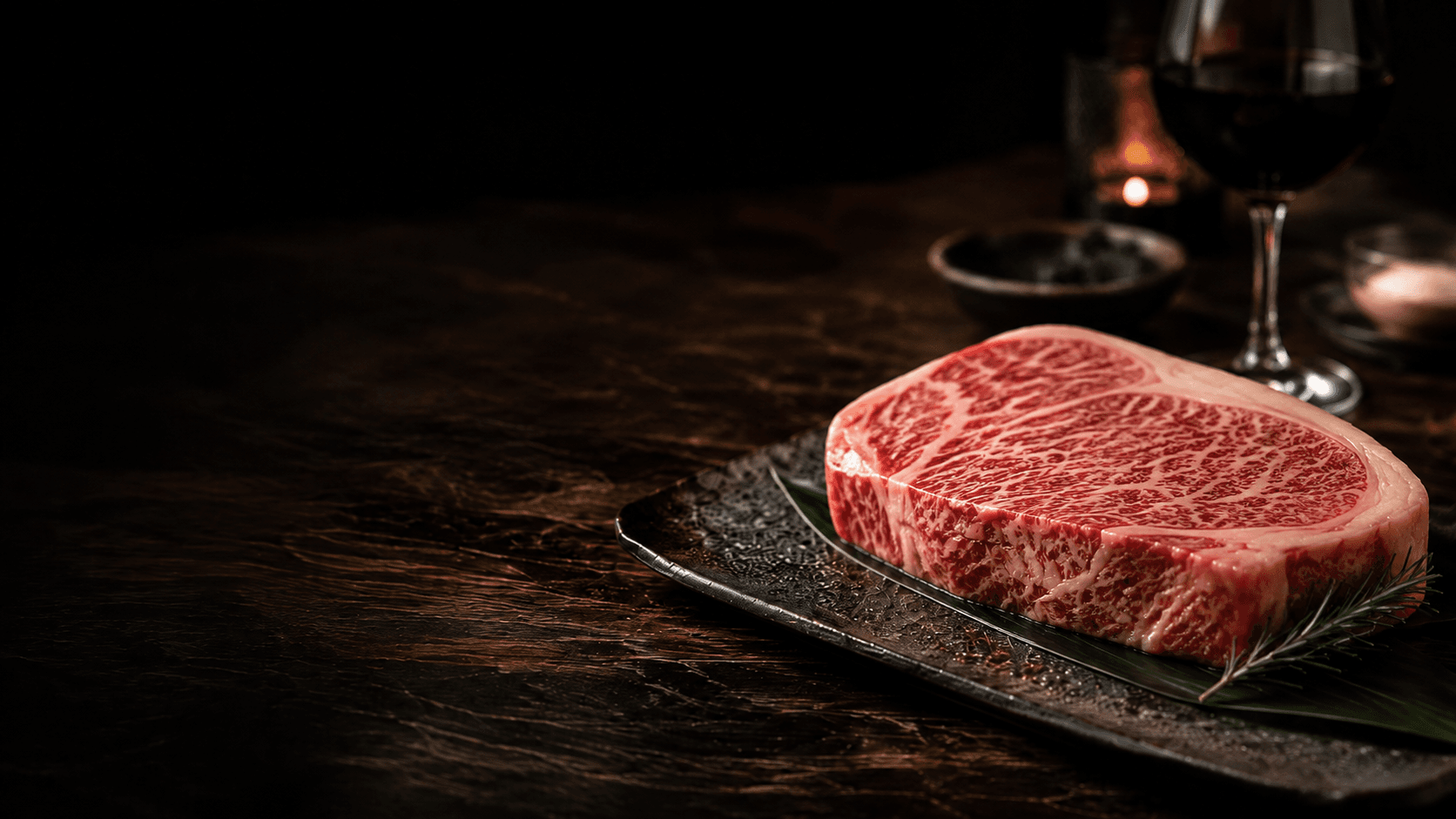 A heavily marbled Japanese Wagyu steak on a dark ceramic plate, with red wine