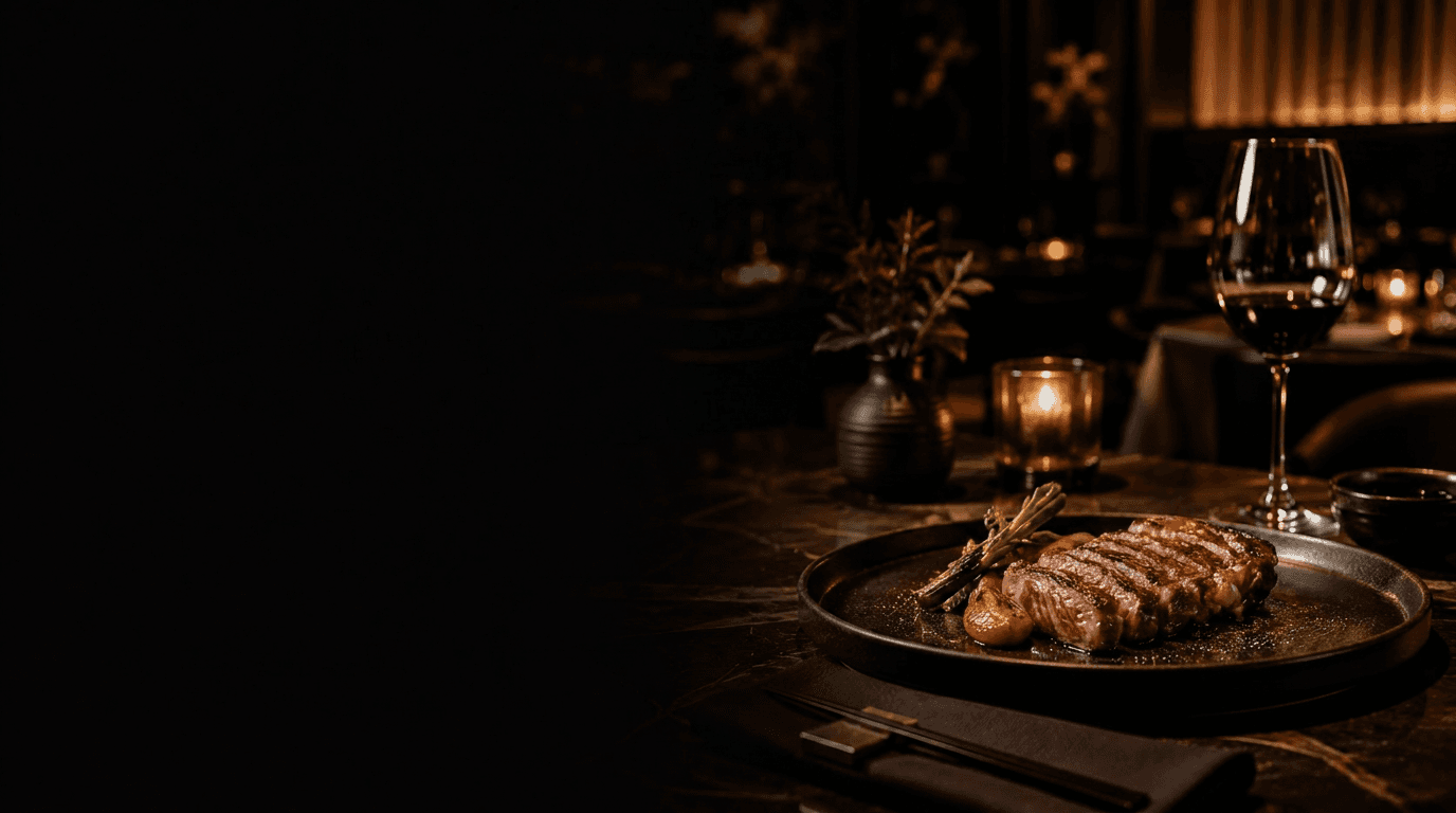 A sliced, seared Wagyu steak on a dark plate beside a glass of red wine in a candlelit fine-dining room