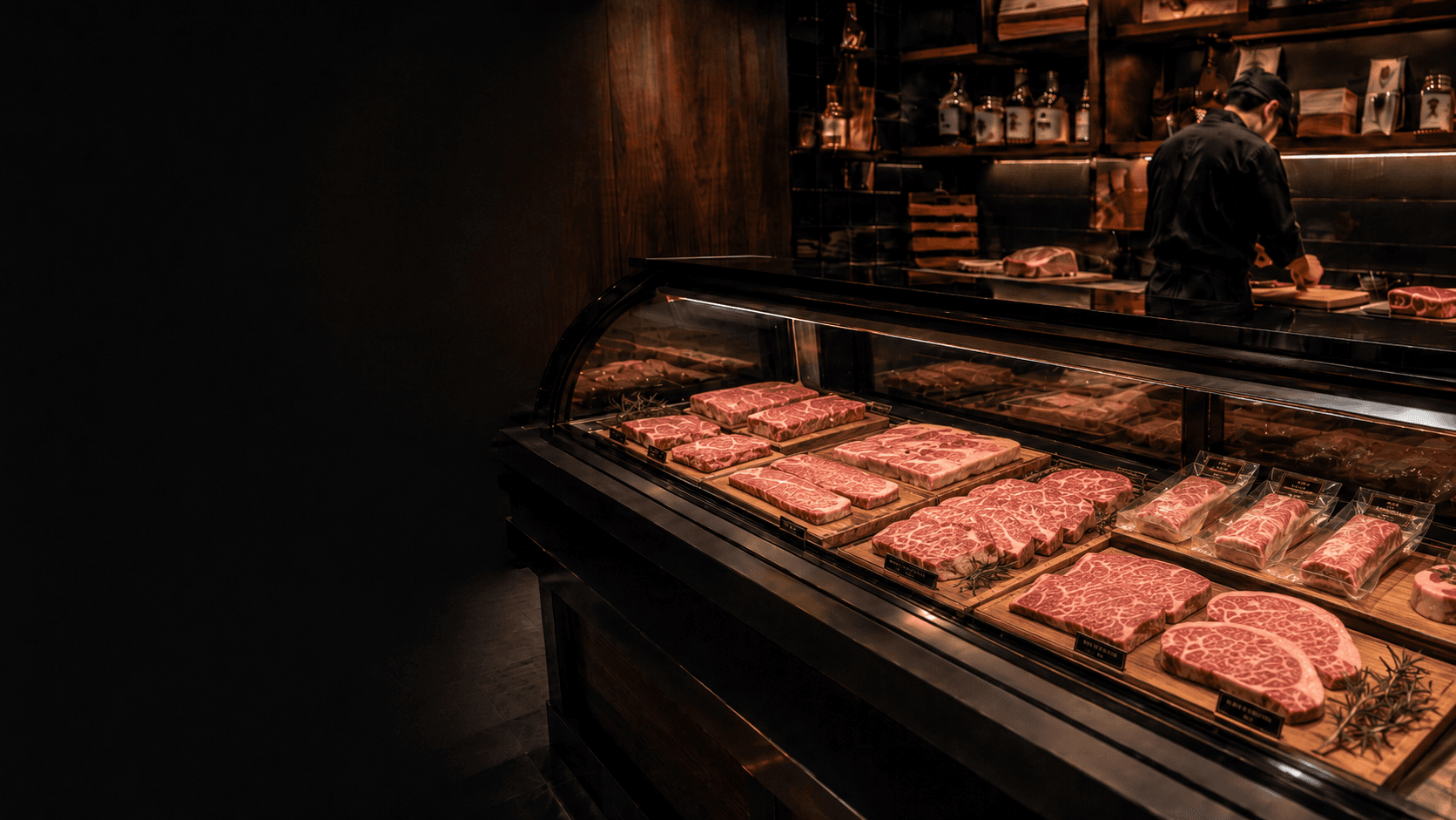 Marbled Wagyu cuts arranged in a butcher's glass display case, with a butcher working behind the counter